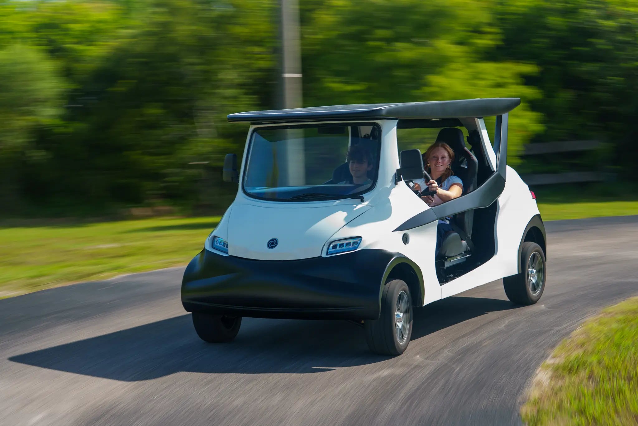 White solar electric INTI car with two people driving on a road surrounded by greenery